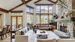 A spacious living room with a stone fireplace, large windows, and wooden beams. - Legendary Lodging at the Ritz Carlton Residences Vail (Vail)