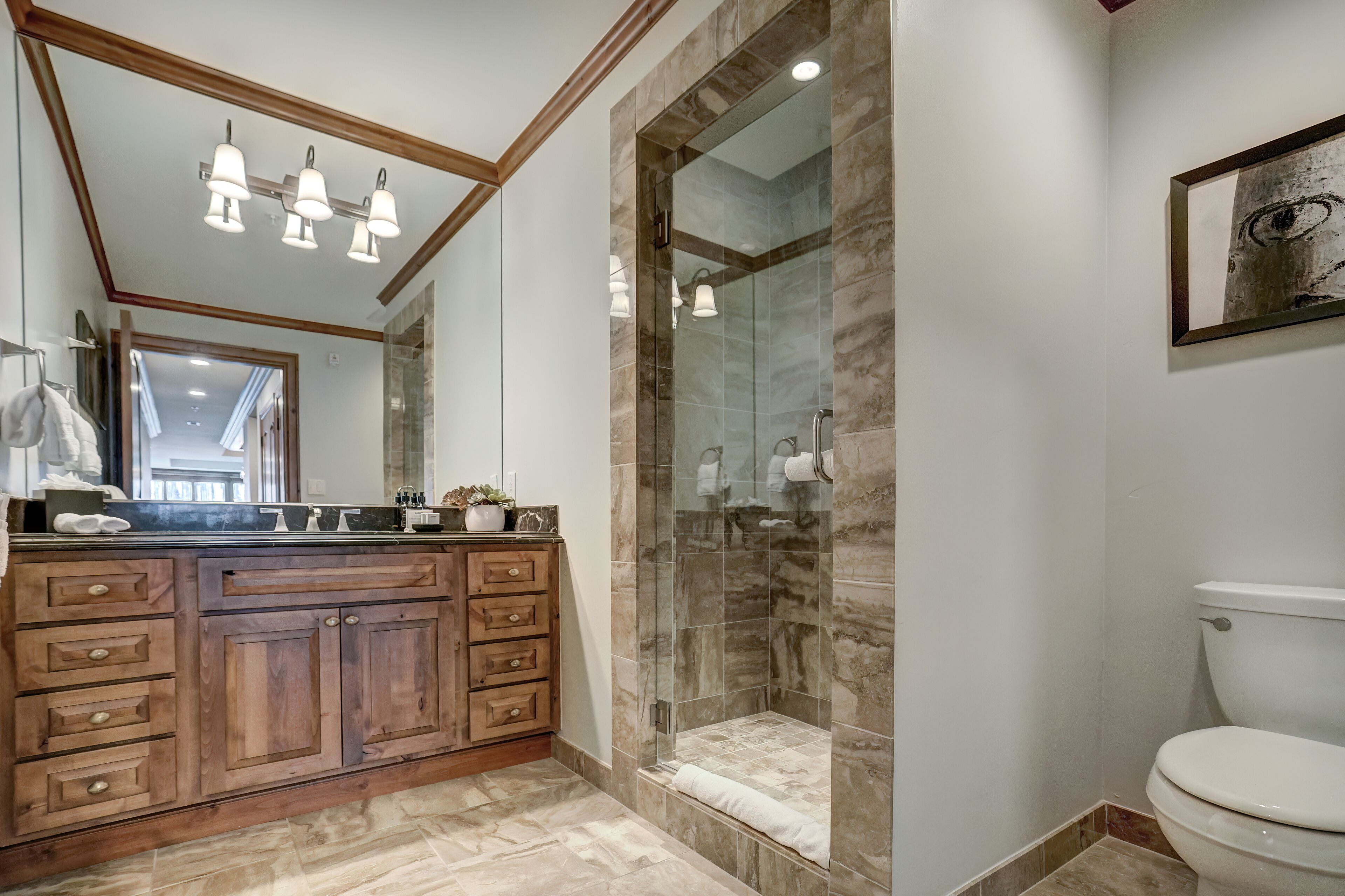 A modern bathroom with a wooden vanity, a glass shower enclosure, and a white toilet.
