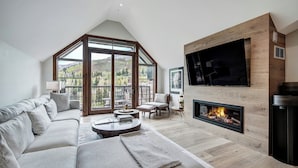 A spacious living room with a large sofa, a fireplace, and a TV mounted on a wooden wall. - Legendary Lodging at the Ritz Carlton Residences Vail (Vail)