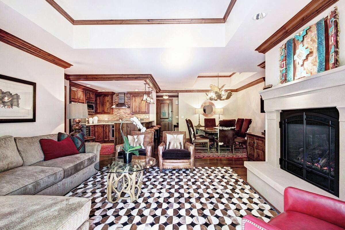 A spacious living room with a patterned floor, a fireplace, and a kitchen area visible through an open doorway.