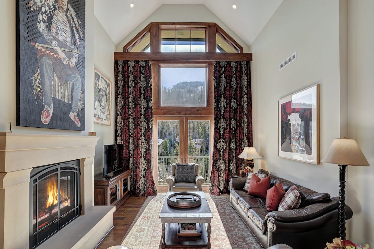 A spacious living room with a fireplace, a large window, and a high ceiling.