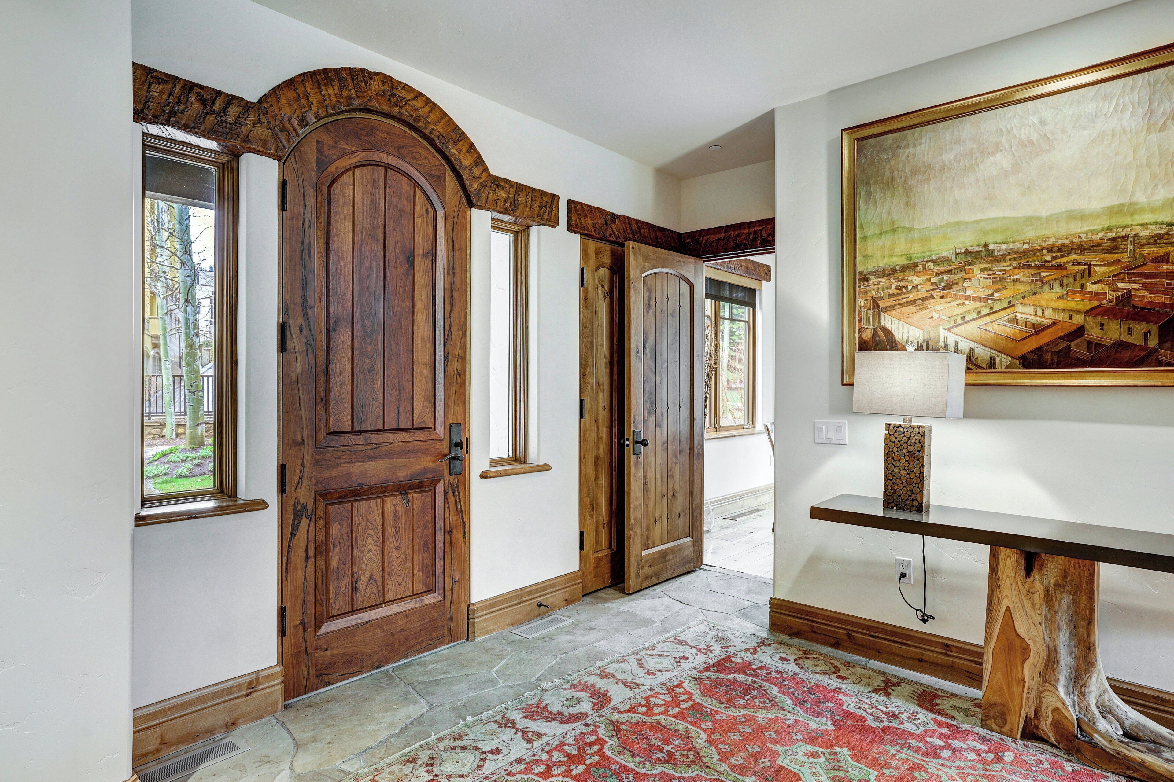 A hallway with wooden doors, a stone floor, and a painting on the wall.