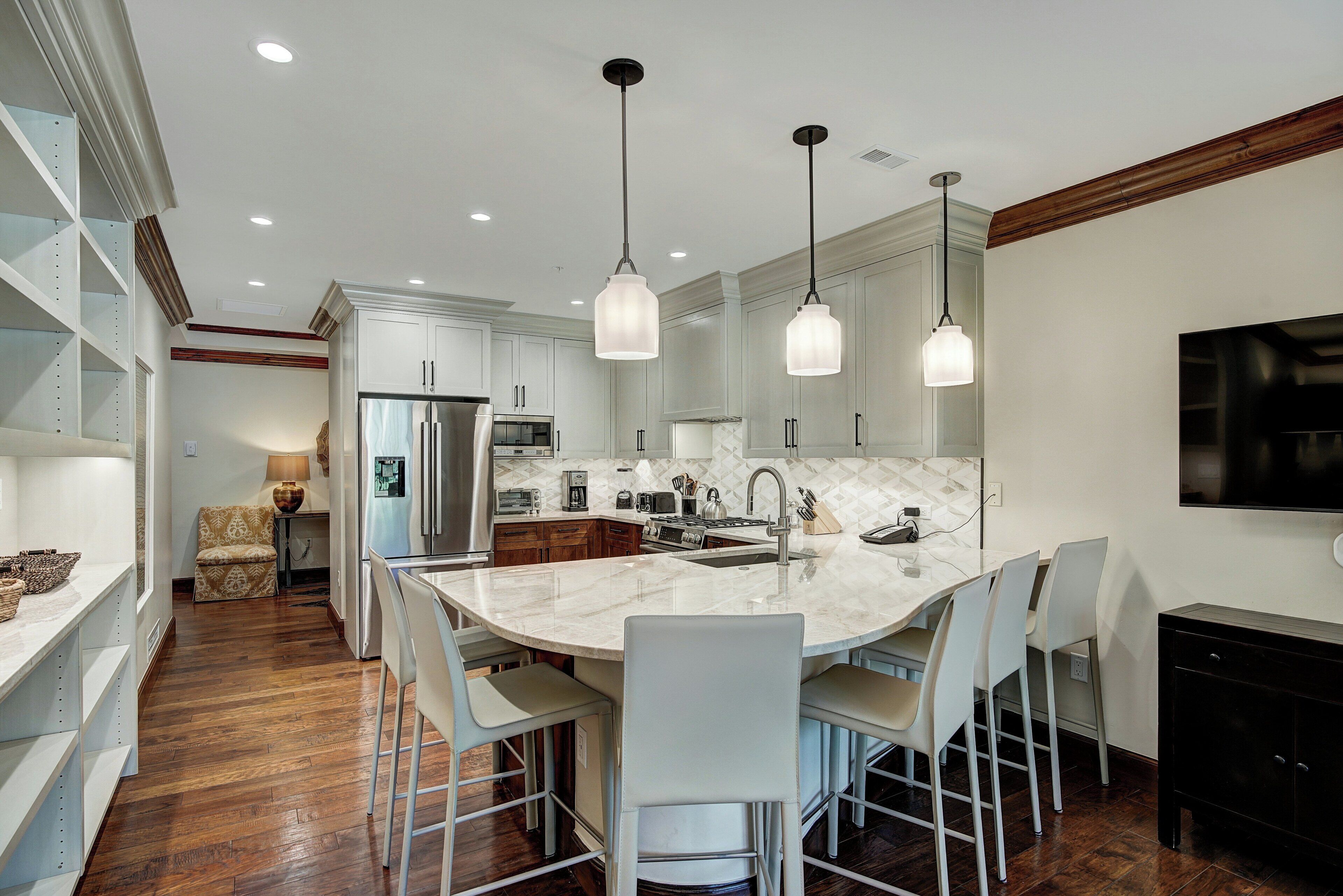 A modern kitchen with a large island, white cabinetry, and pendant lighting.