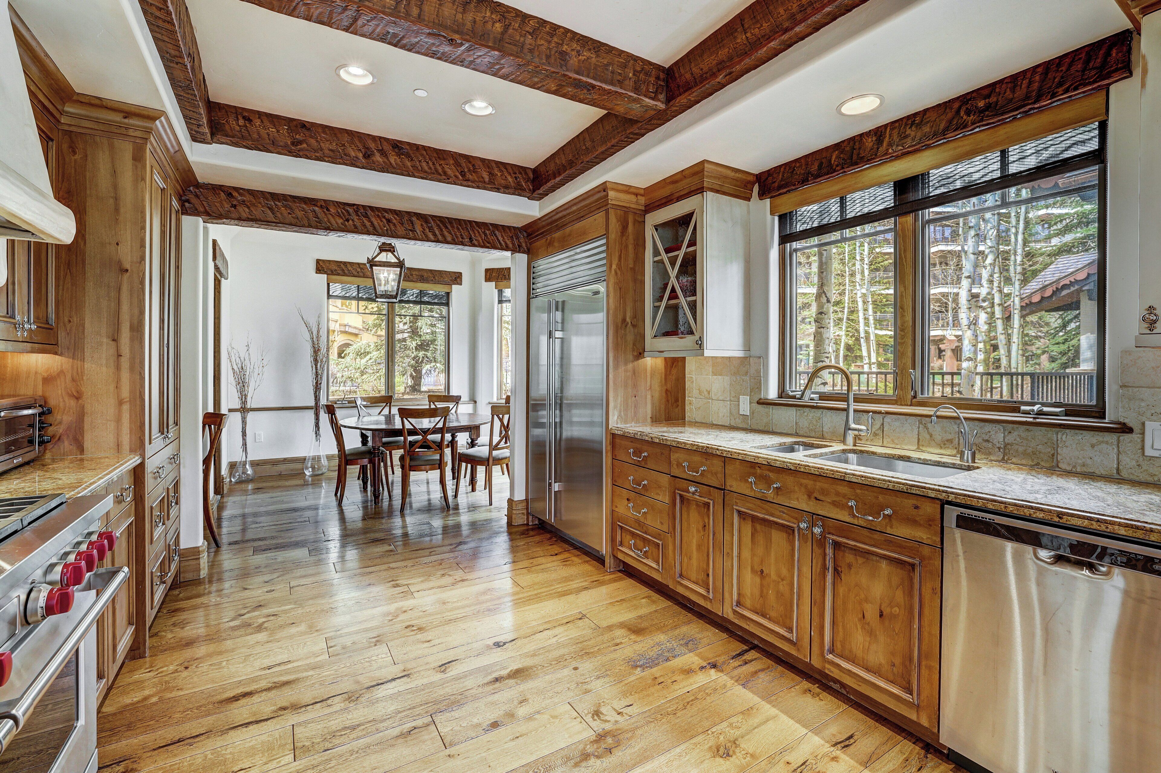 Una cocina amplia con gabinetes de madera, electrodomésticos de acero inoxidable y ventanas grandes que ofrecen vistas al exterior.