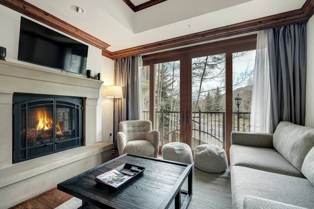 A living room with a fireplace, a sofa, a coffee table, and a view of the outdoors.