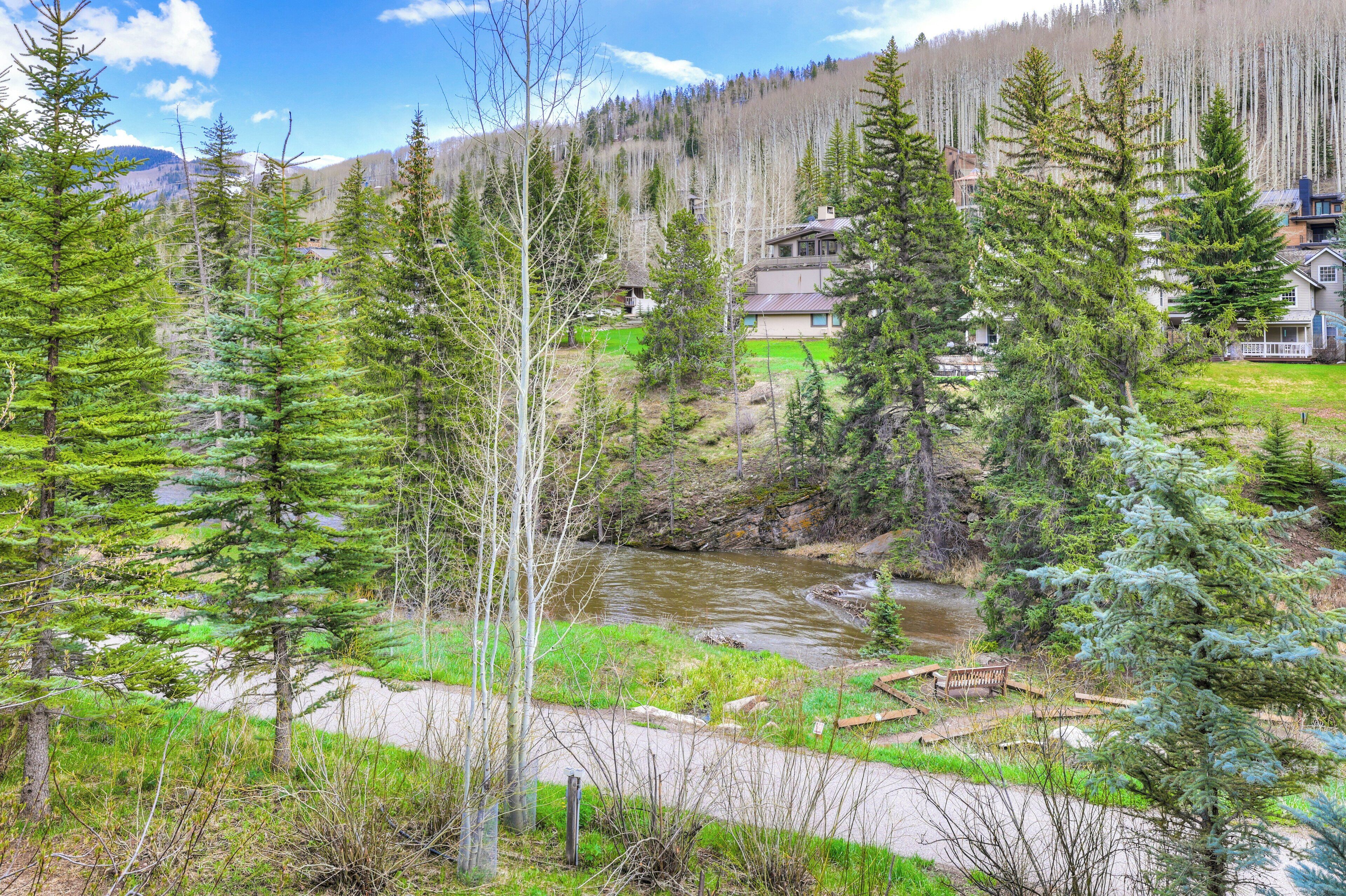 A river flowing through a forested area with houses in the background.