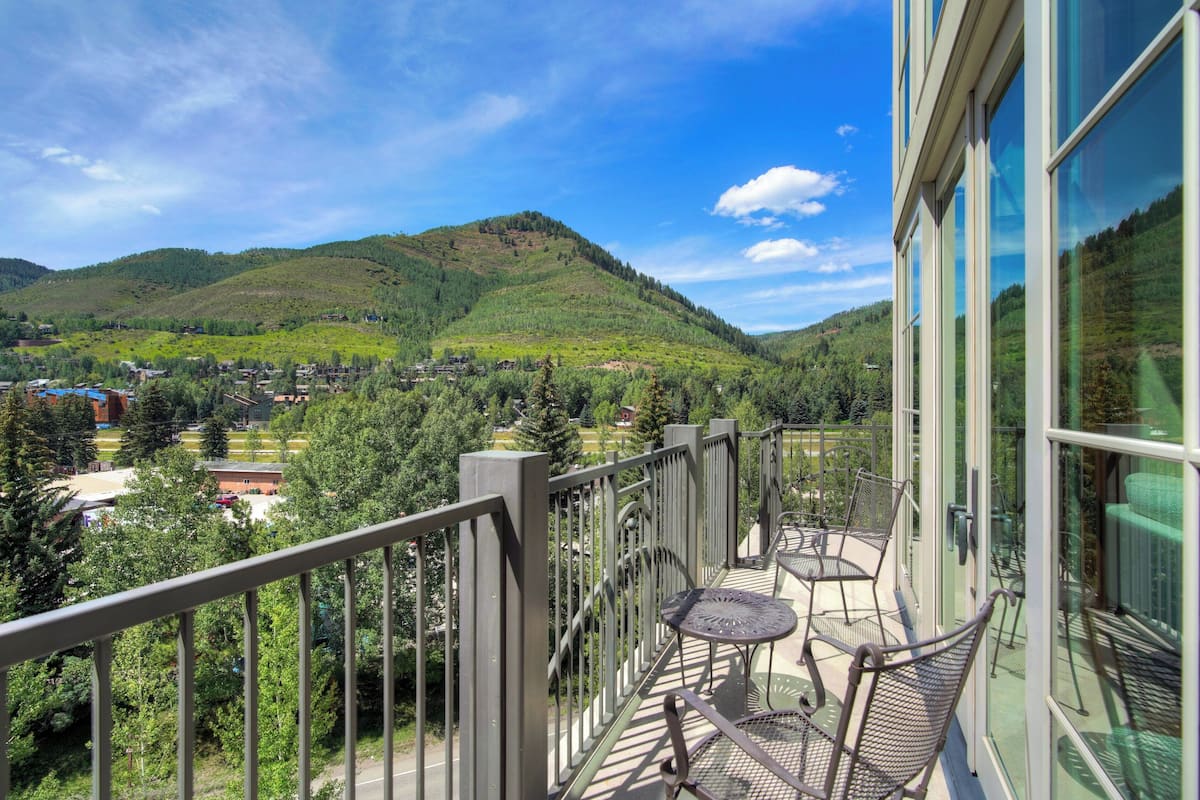 A balcony with a view of a mountainous landscape, a glass wall, and outdoor furniture.
