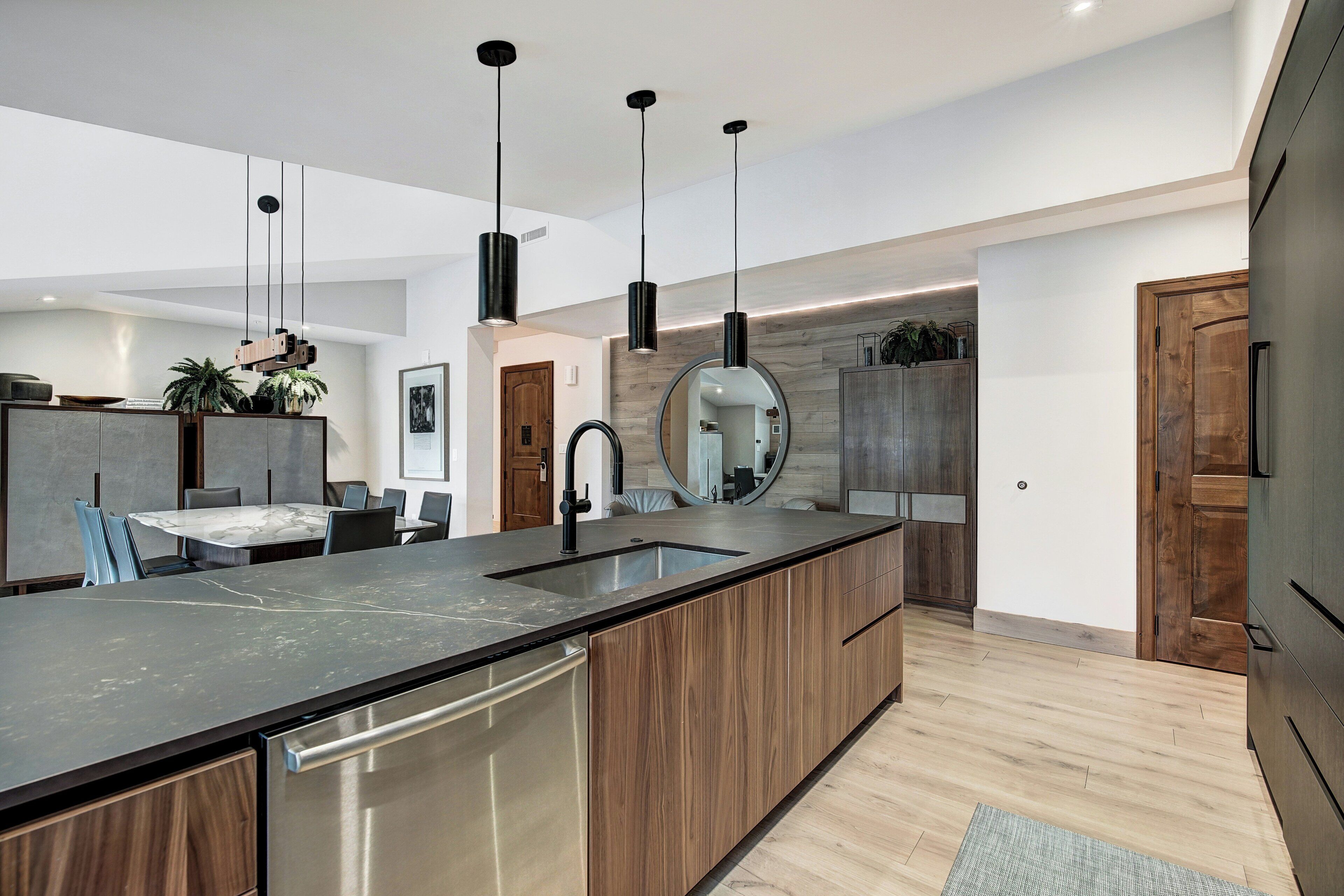 Une cuisine moderne dotée d’un grand îlot central, d’appareils électroménagers intégrés, de luminaires suspendus et d’un revêtement en bois.
