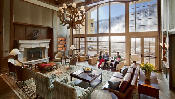 A spacious living room with a fireplace, comfortable seating, and a large window offering a view of a snowy landscape. - Legendary Lodging at the Ritz Carlton Residences Vail (Vail)