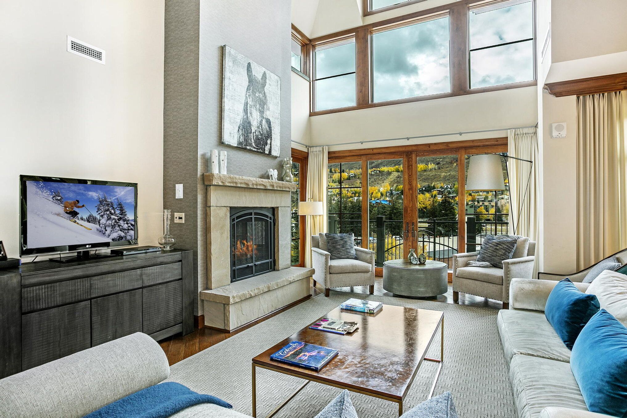 Un salón espacioso con chimenea, asientos cómodos, televisor y grandes ventanas con vistas al exterior.