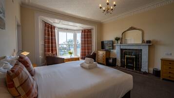 Une chambre d’hôtel avec un grand lit, une cheminée, une télévision et une fenêtre avec des rideaux.