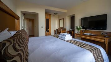 A hotel room with a large bed, a wooden desk, a flat-screen TV, and a bathroom visible through an open door.