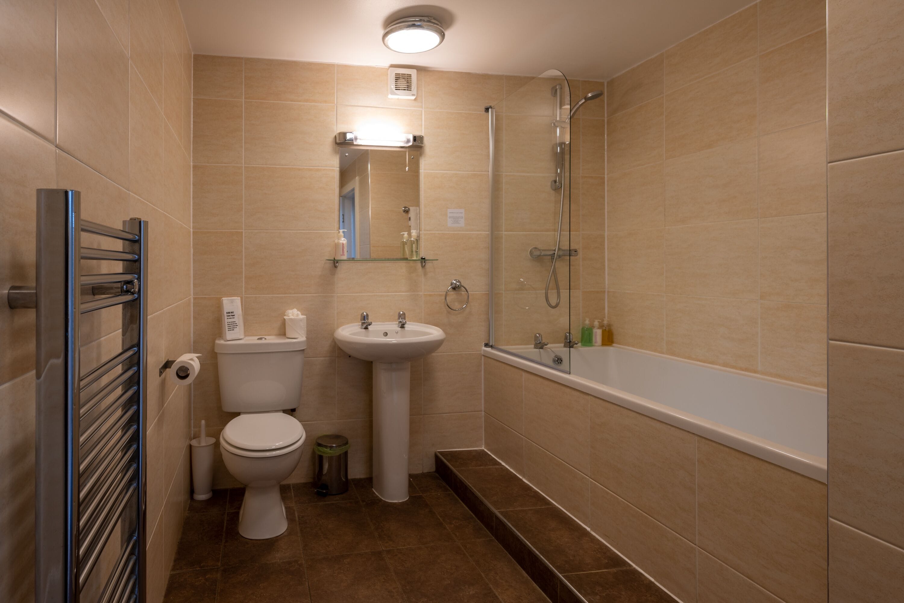 Un baño con inodoro, lavabo, ducha y un estante de vidrio con artículos de aseo.