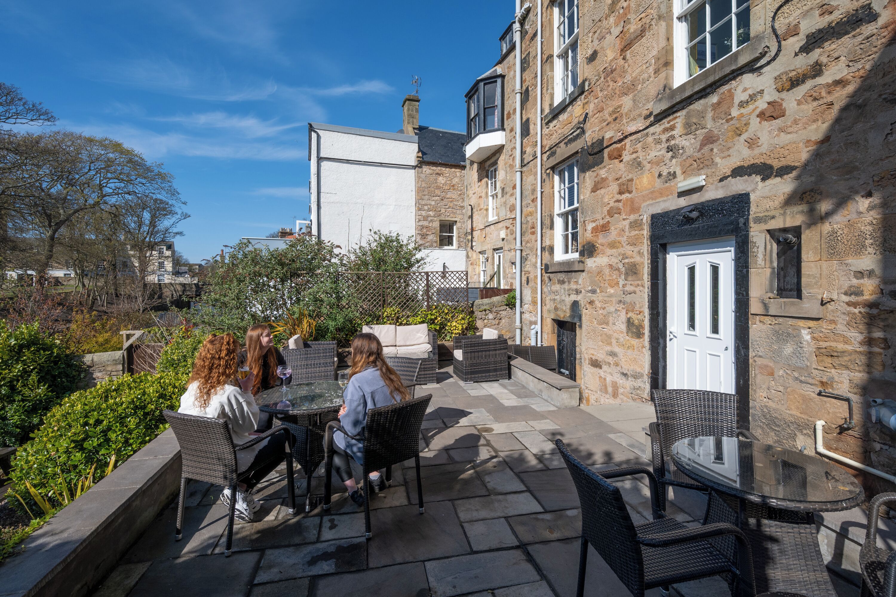 Une terrasse extérieure avec un sol en pierre, des meubles en osier et une table en verre.