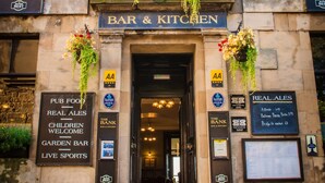 Un bâtiment en pierre avec une enseigne indiquant « BAR ET RESTAURANT » et diverses autres enseignes signalant des services tels que « REPAS DE PUB », « BIÈRES ARTISANALES » et « DIFFUSION D’ÉVÉNEMENTS SPORTIFS EN DIRECT ».