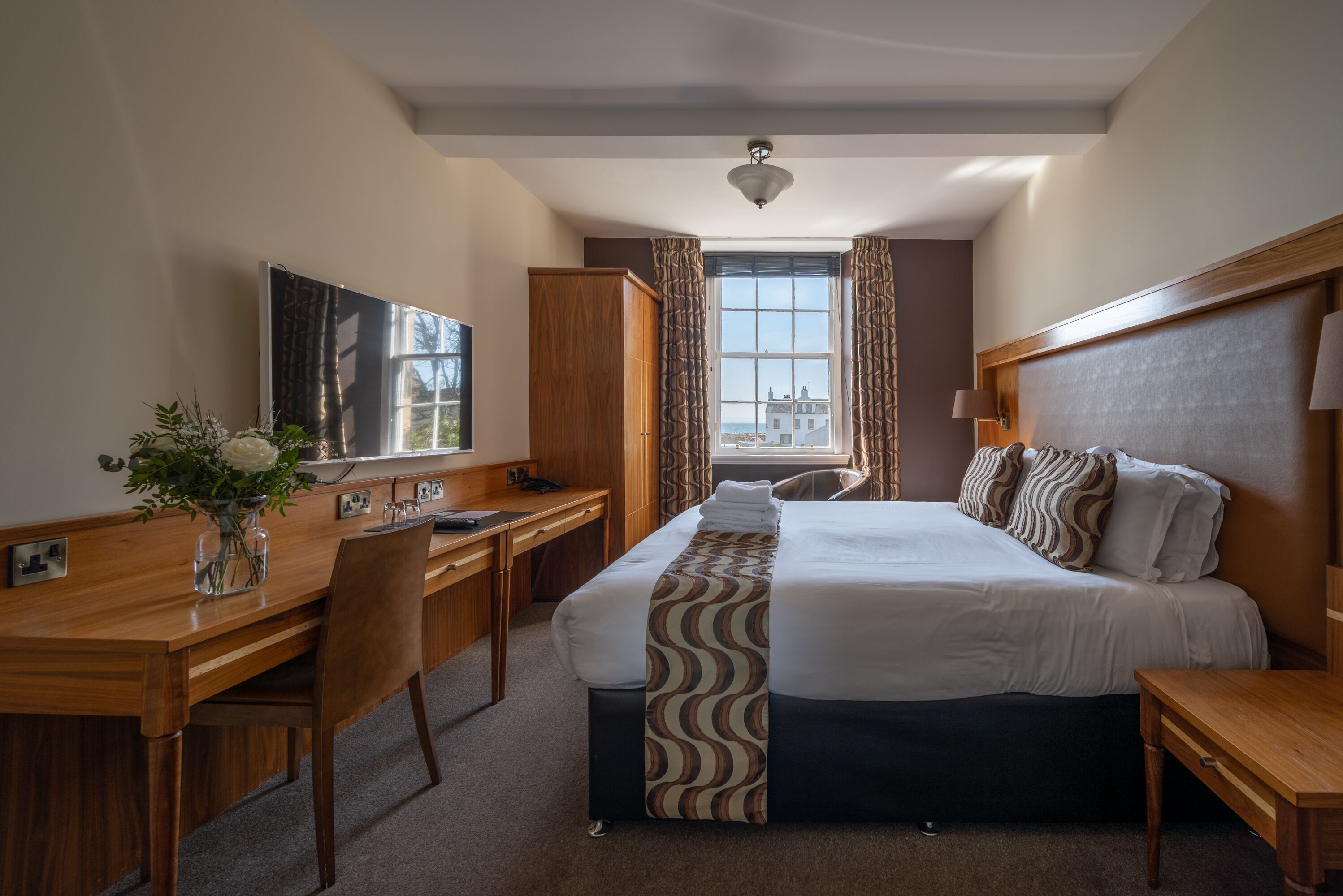 Habitación de hotel con cama, escritorio, silla, televisor y vistas a edificios por la ventana.