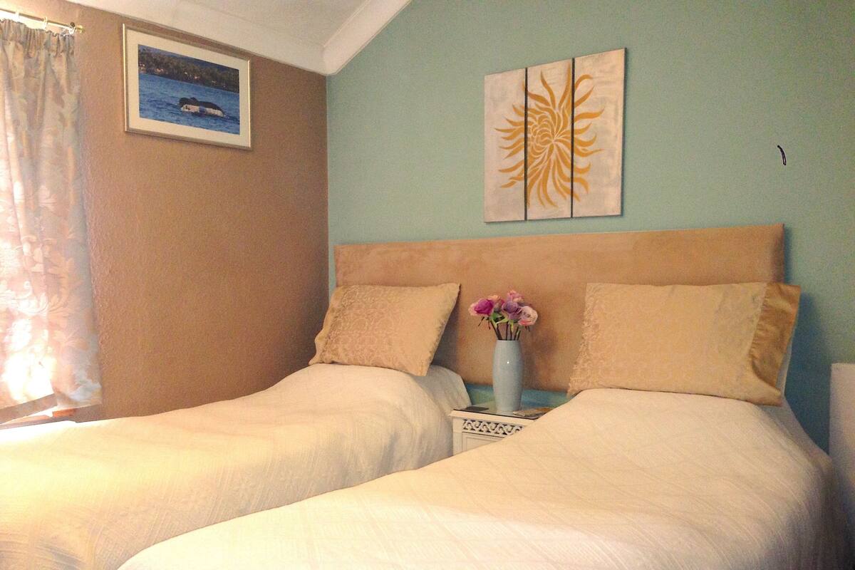 A bedroom with two beds, a vase with flowers, and a framed picture on the wall.