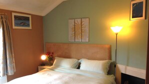 Un dormitorio con cama, mesita de noche, lámpara y una obra de arte en la pared.