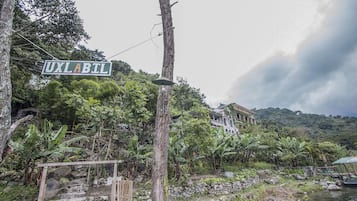 Uma placa com a inscrição 'UXLABTL' em uma área verde e exuberante, com uma escadaria de pedra que leva a um edifício.