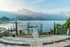 A lakeside walkway leading to a covered seating area with a view of mountains and boats. - Eco Hotel Uxlabil Atitlan (San Juan La Laguna)