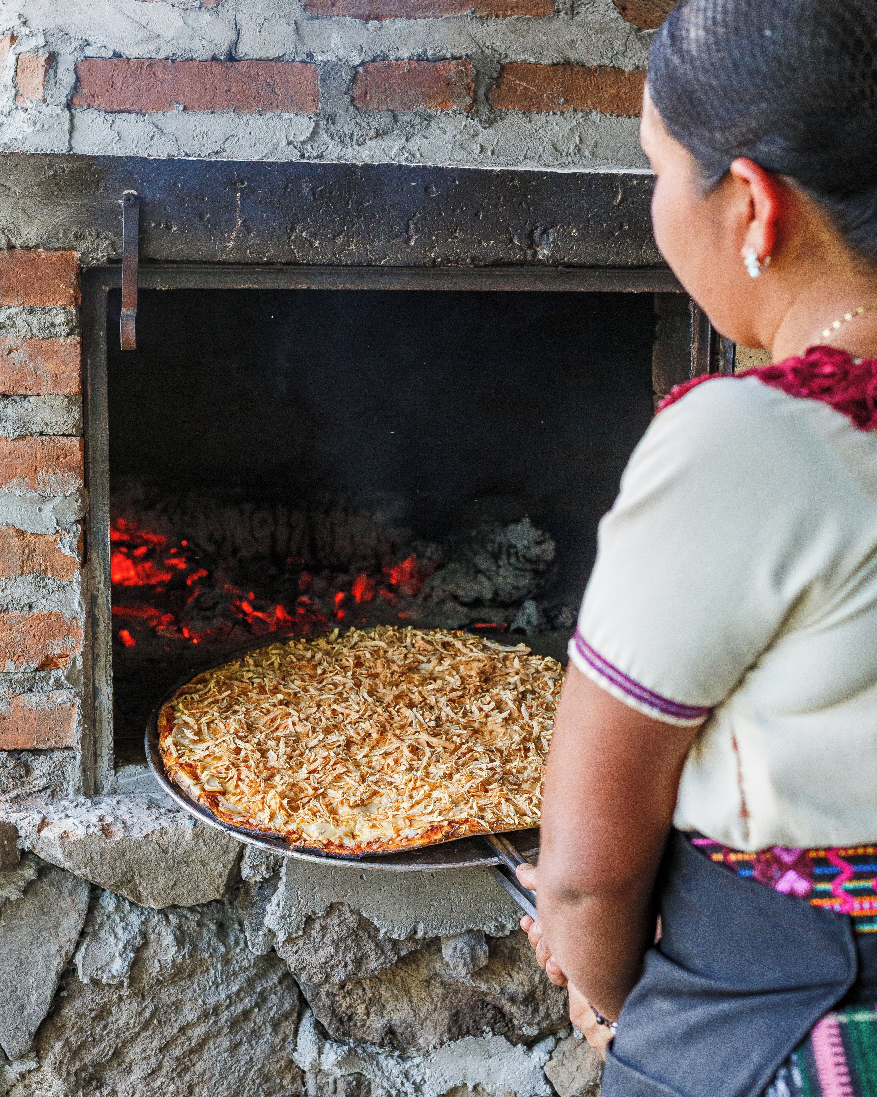 A woman placing a pizza in a brick oven.