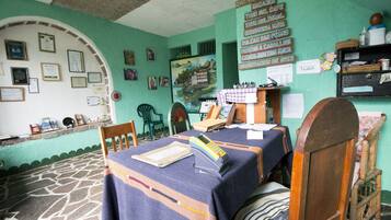 A room with a stone floor, wooden furniture, and a table with a blue tablecloth. There are framed certificates on the wall and a painting depicting a landscape.