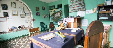 A room with a stone floor, wooden furniture, and a table with a blue tablecloth. There are framed certificates on the wall and a painting depicting a landscape.