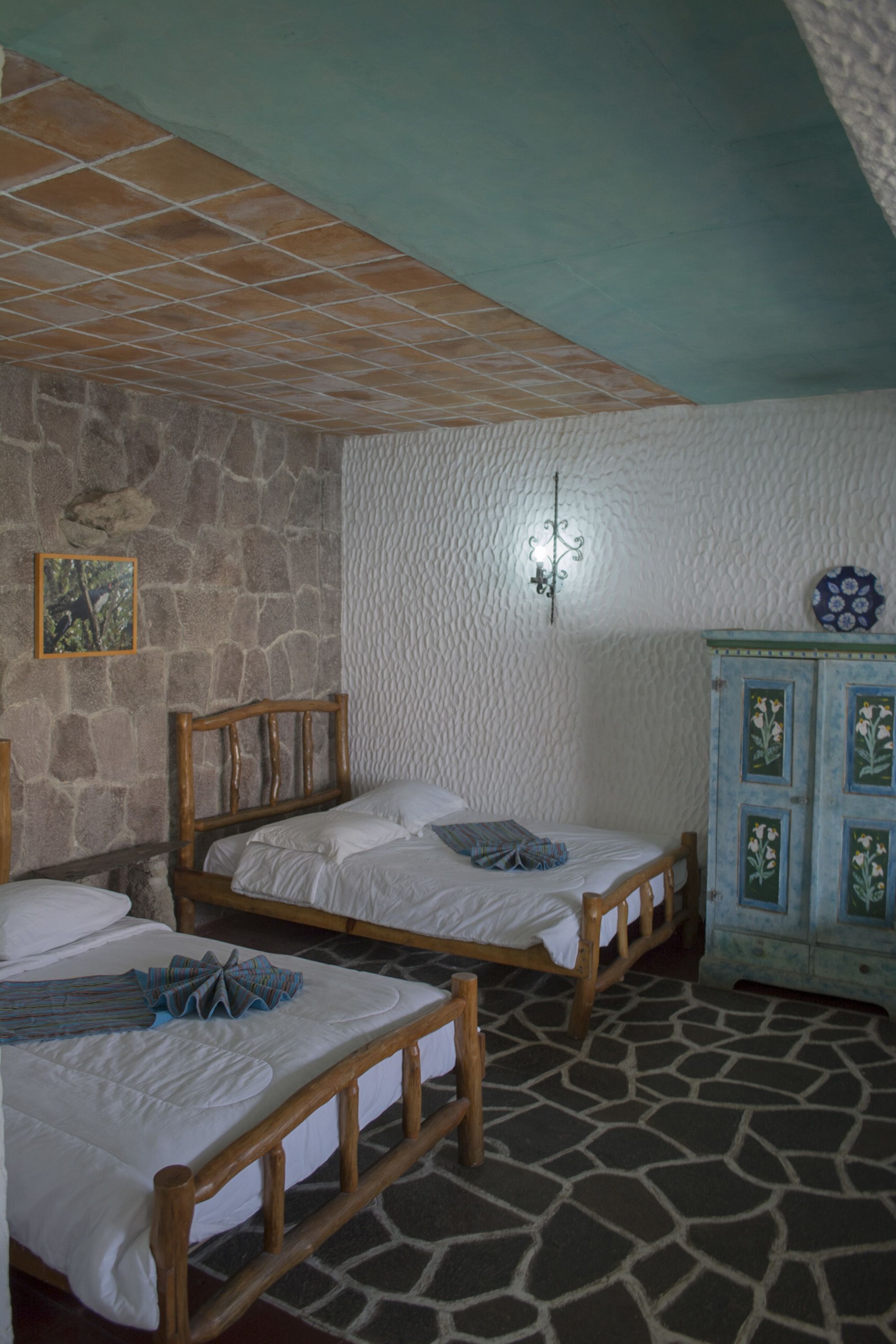 A room with two wooden beds, a stone wall, a textured white ceiling, and a cabinet with floral designs.