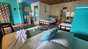 A hotel room with two beds, a small table, a chair, a bathroom with a mirror, and a colorful wall.