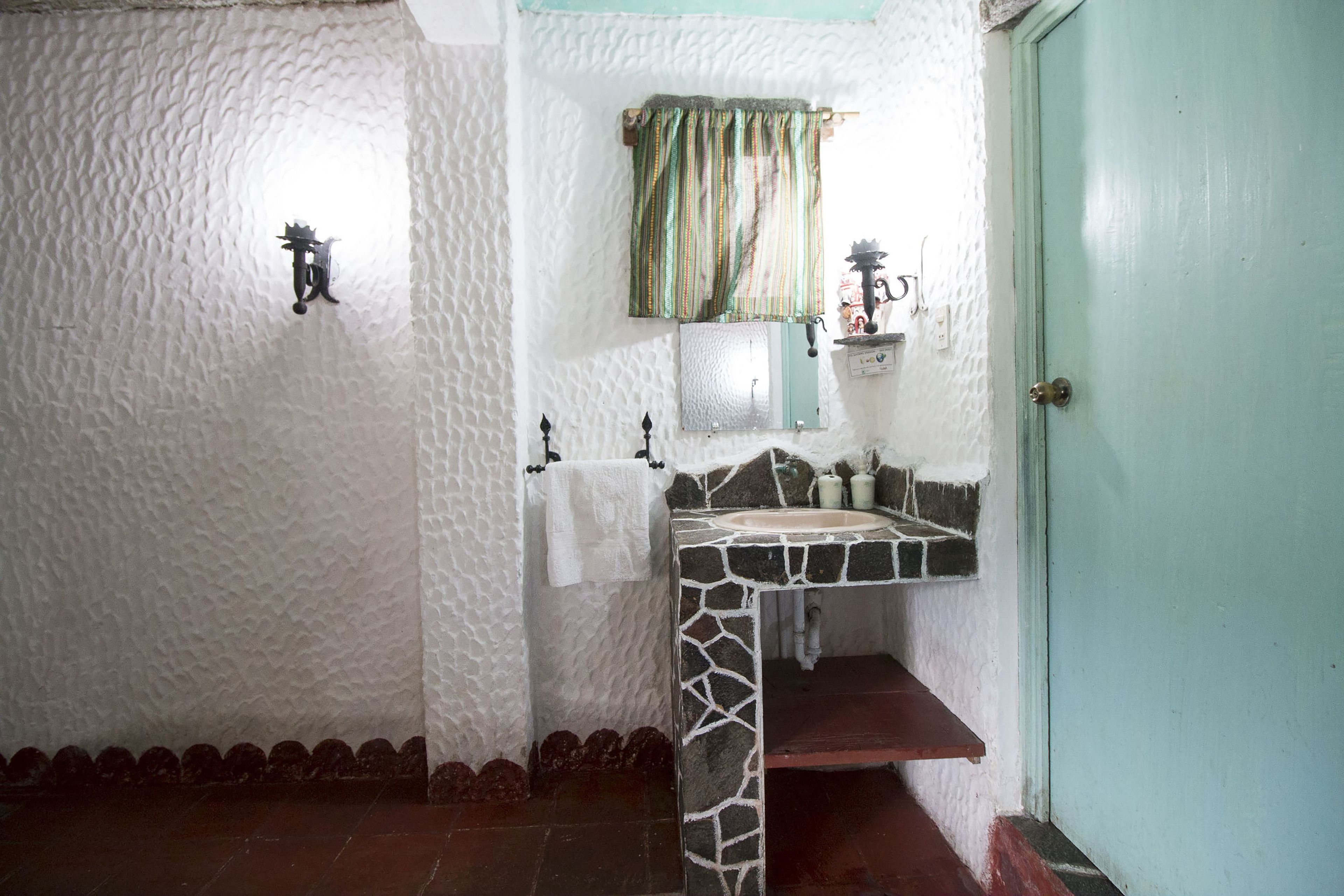 Une salle de bain avec un lavabo en pierre, un miroir, une serviette accrochée au mur et une porte.