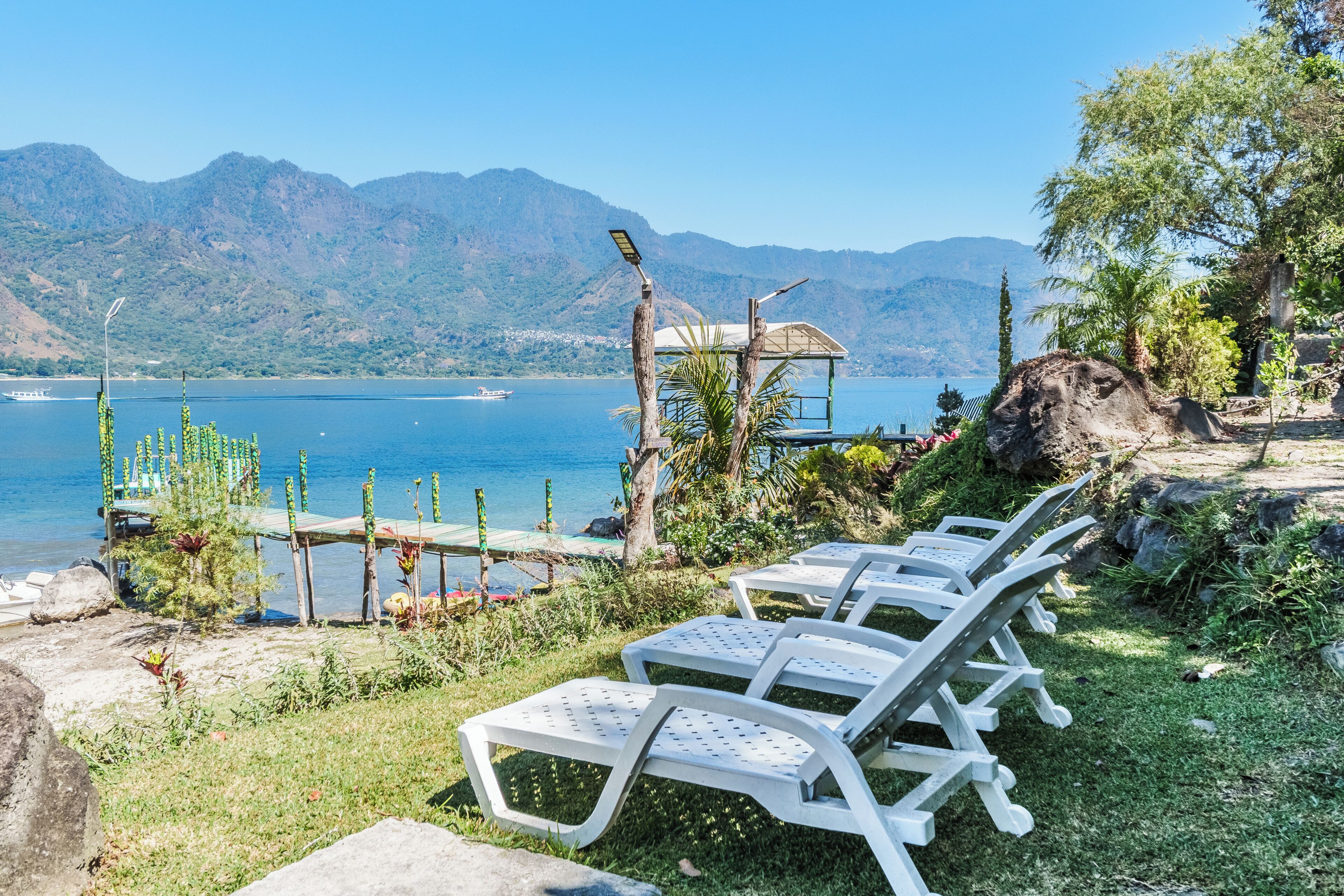 Outdoor lounge chairs by a lake with mountains in the background.