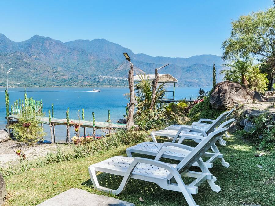 Des fauteuils de salon installés à l’extérieur, au bord d’un lac, avec des montagnes en arrière-plan.