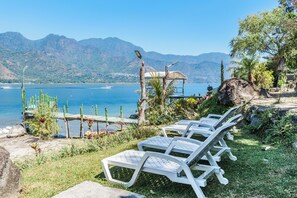 Outdoor lounge chairs by a lake with mountains in the background. - Eco Hotel Uxlabil Atitlan (San Juan La Laguna)