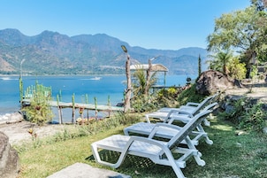Sillones de exterior junto a un lago con montañas al fondo.