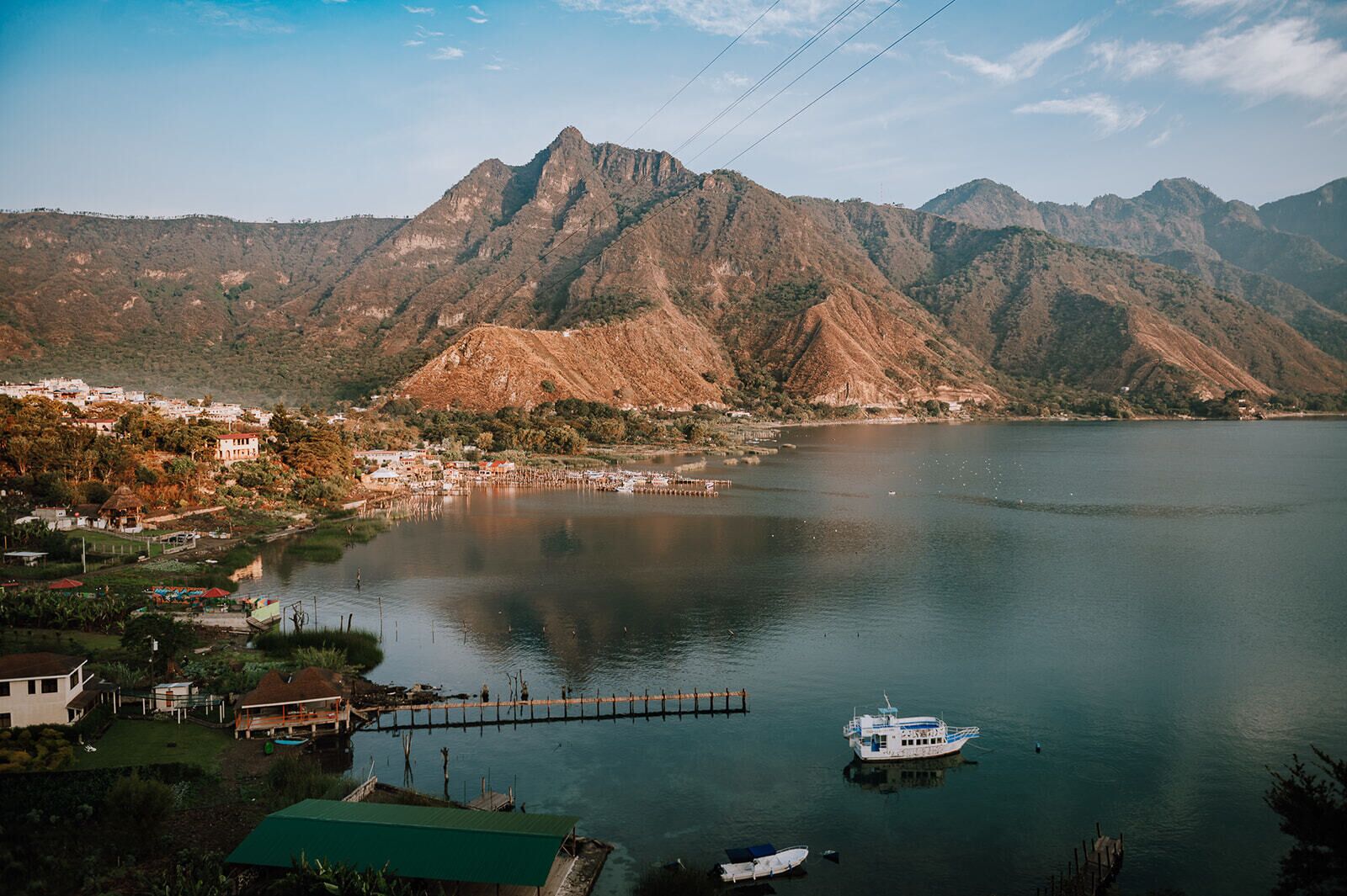 Un lago con montañas al fondo, un muelle y un bote.