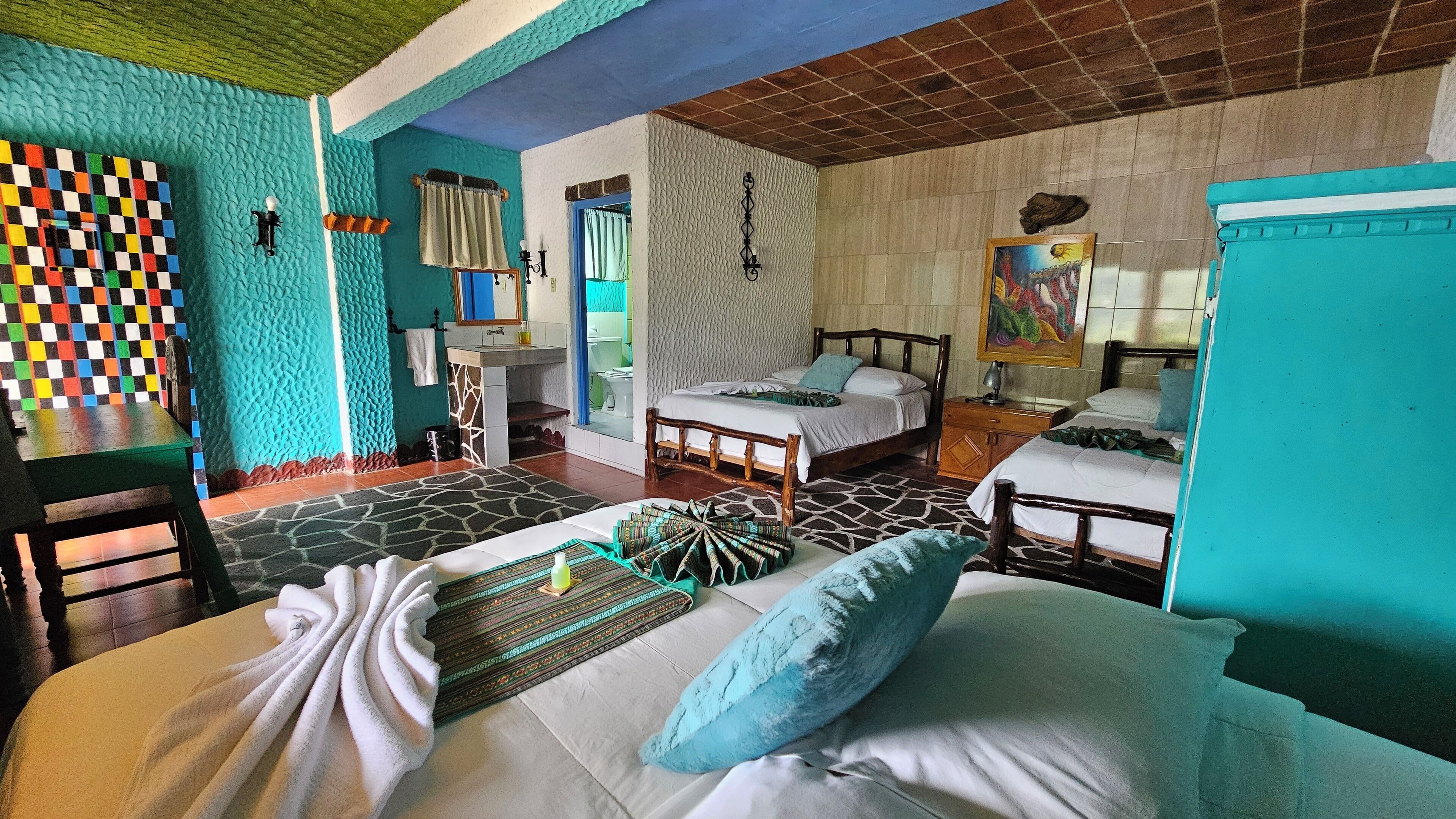 A room with two beds, a small table, and a chair. There is a window with curtains and a wall with a textured pattern.