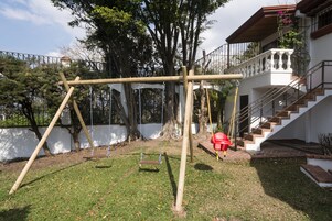 Un columpio de madera en un césped con un edificio blanco y una escalera.