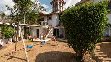 A residential property with a swing set, a staircase leading to a balcony, and a large bush.