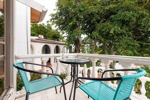 A balcony with two turquoise wicker chairs and a glass table, overlooking a courtyard with a white building and trees. - Posada El Quijote (San Rafael)