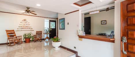 A reception area with a wooden reception desk, a ceiling fan, potted plants, and a staircase leading to another floor.