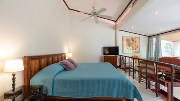 A spacious bedroom with a large bed, a ceiling fan, a TV, and a balcony with a view.