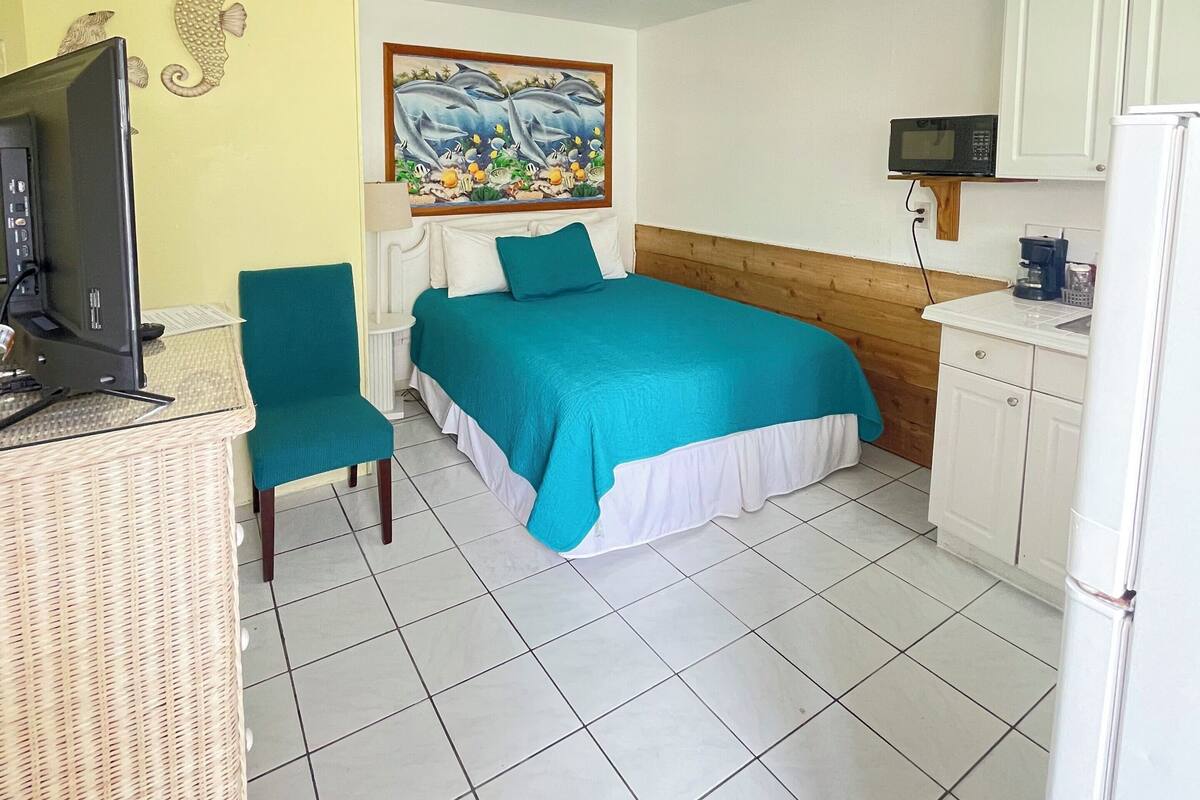 A room with a bed, a chair, a desk with a computer, a microwave, and a refrigerator.