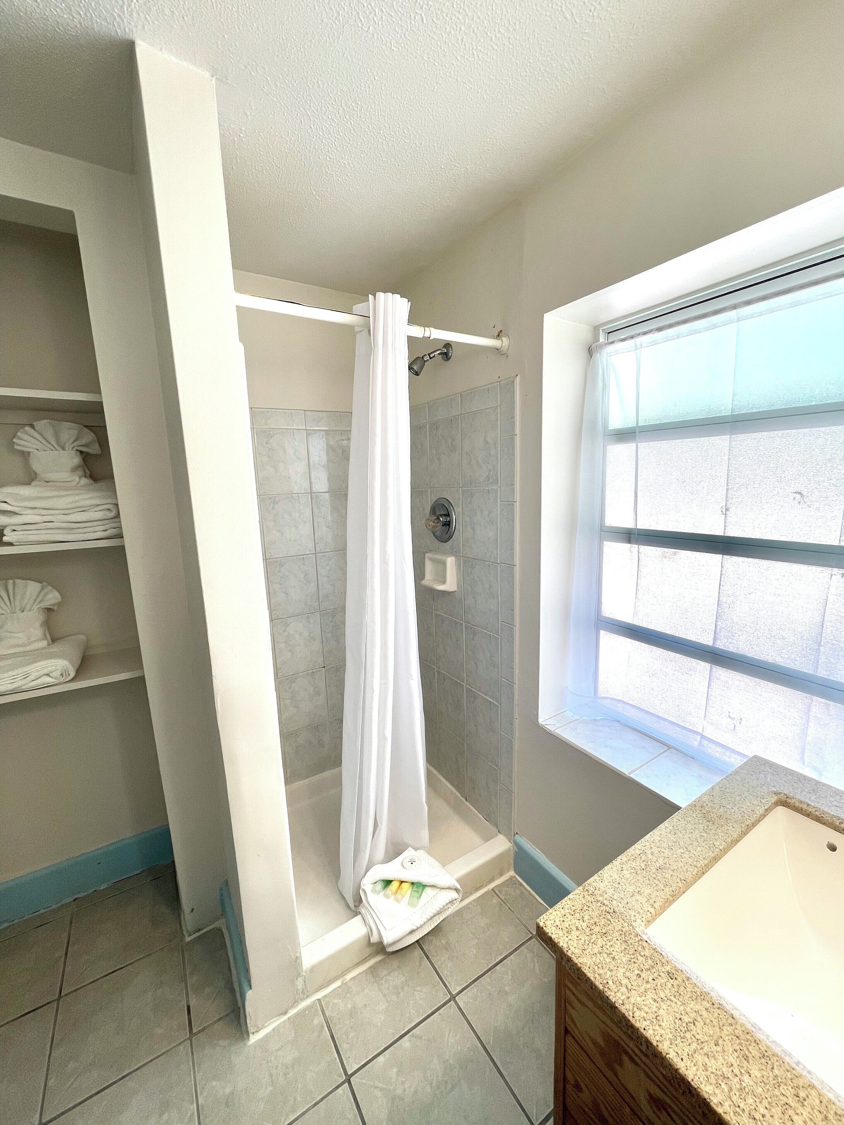 Un baño con ducha, lavamanos y ventana.