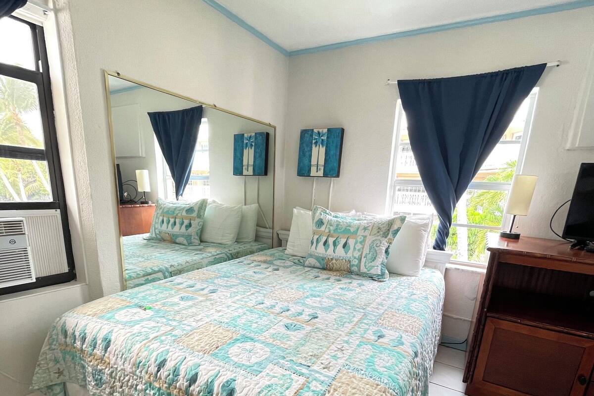 A bedroom with a large bed, a dresser, a mirror, and a window with curtains.