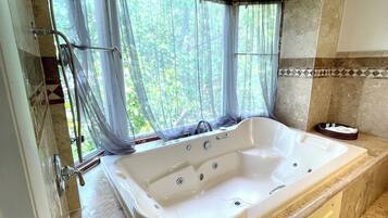 Une salle de bain avec une grande baignoire, une douche et une fenêtre avec des rideaux.