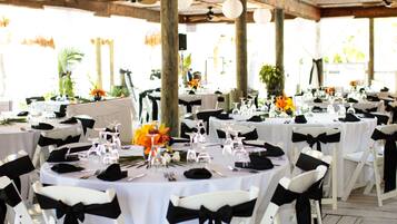 Un salón de banquetes con mesas redondas, sillas blancas y cintas negras. Las mesas están dispuestas con cristalería, platos y cubertería.