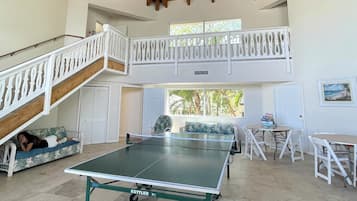 A spacious room with a ping pong table, a ceiling fan, and a staircase leading to an upper level.