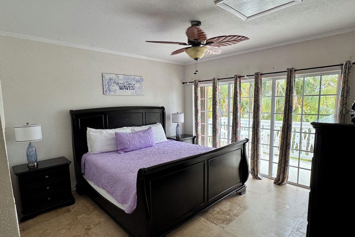 A bedroom with a bed, a ceiling fan, a window with curtains, and a wall decoration.