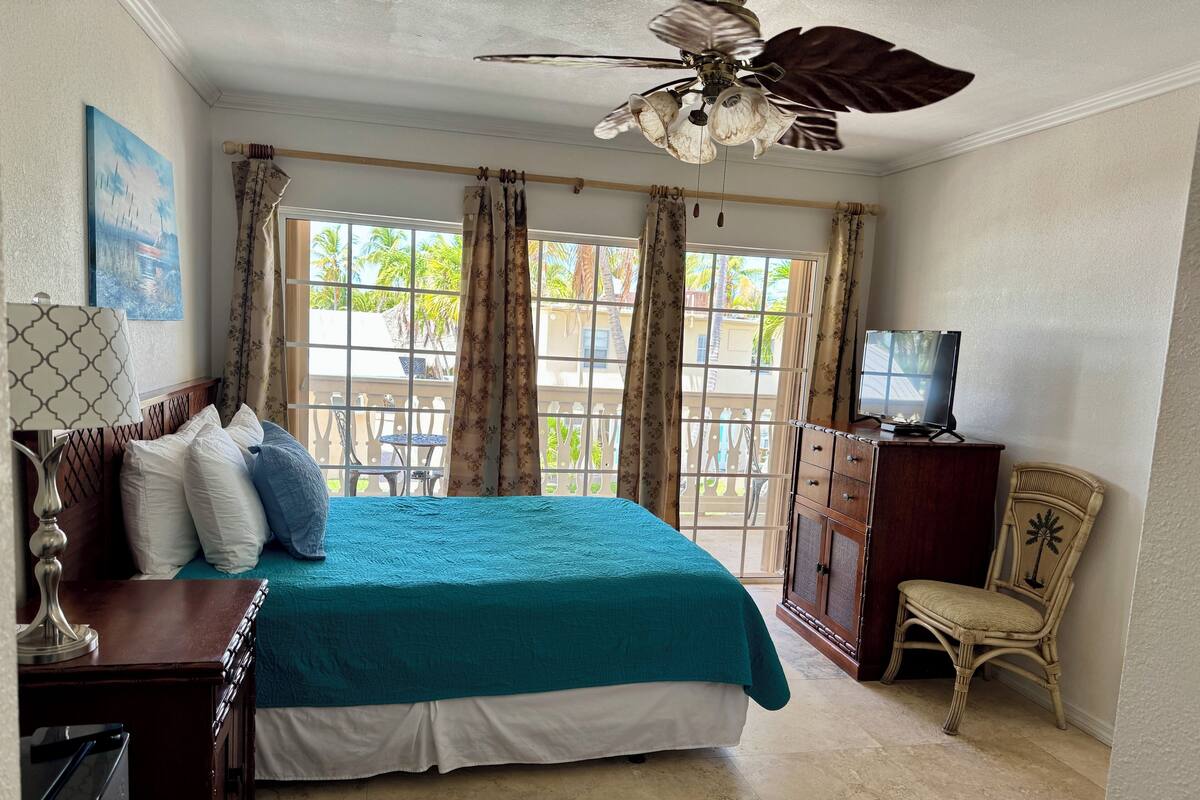 A bedroom with a bed, a television, a wooden cabinet, a chair, and a ceiling fan.