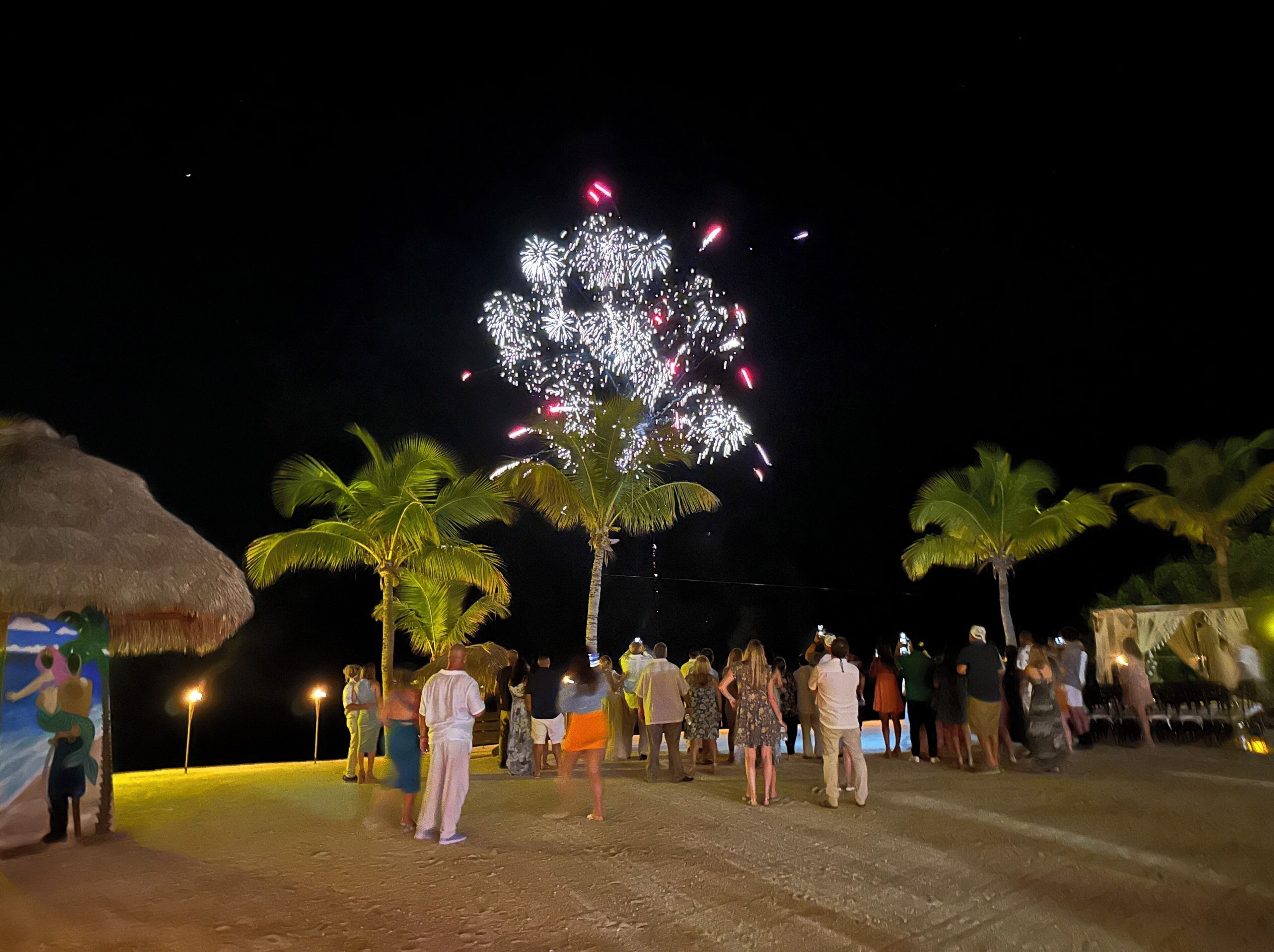 Reunión en la playa con gente mirando fuegos artificiales.